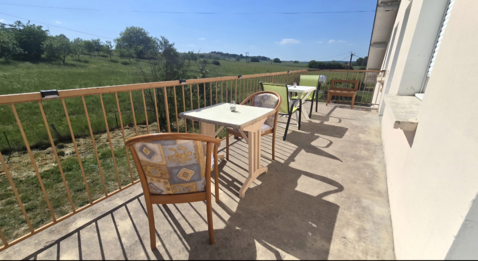 Balcon commun aménagé avec tables et vue sur le terrain verdoyant